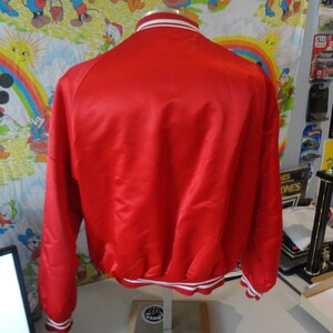 May include: A red satin bomber jacket with white and red striped trim around the collar, cuffs, and hem.