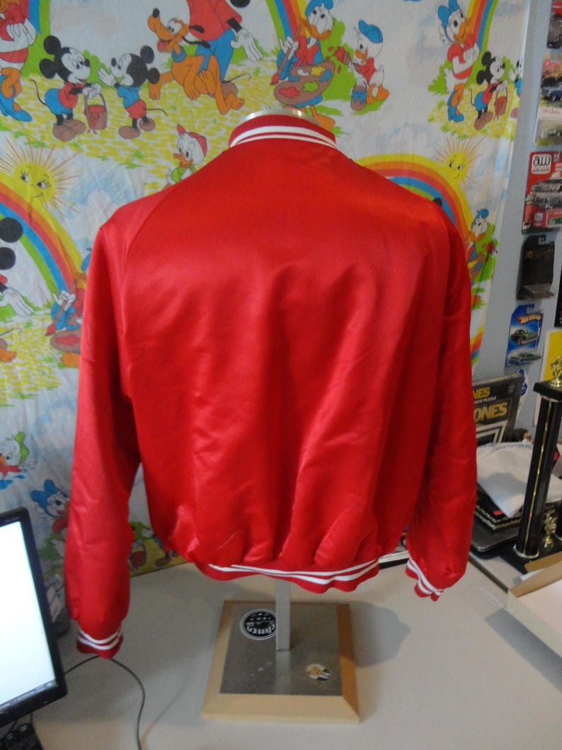 May include: A red satin bomber jacket with white and red striped trim around the collar, cuffs, and hem.
