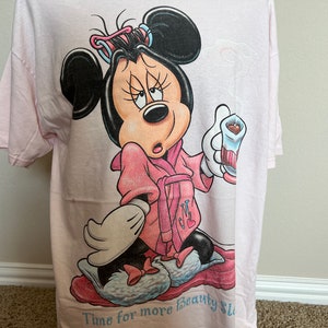 May include: Light pink t-shirt featuring a cartoon Minnie Mouse in a pink robe and curlers, holding a drink. The text "Time for more beauty sleep" is at the bottom of the shirt. The shirt is made of a soft material.