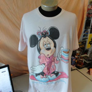May include: A light pink t-shirt featuring a cartoon Minnie Mouse in a pink robe, holding a cup. The graphic includes the text "Time for more Beauty Sleep". The shirt is displayed on a mannequin.