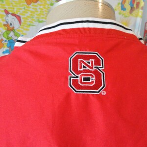 May include: Red jacket with a white and black striped collar and a large embroidered "NC" logo on the back.
