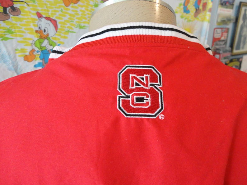 May include: Red jacket with a white and black striped collar and a large embroidered "NC" logo on the back.