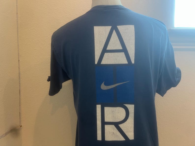 Puede incluir: Una camiseta azul marino con un gr&aacute;fico blanco de "AIR" en la espalda. La "A" y la "R" est&aacute;n en cajas, y la "I" es una caja azul con un swoosh blanco de Nike.