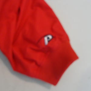 May include: Red short-sleeved shirt with a white "P" logo on the sleeve.