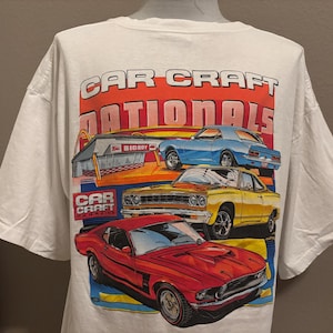 May include: White t-shirt featuring a colorful graphic of classic cars with the text "CAR CRAFT NATIONALS". The design includes a red, yellow, and blue car, and the text "CAR CRAFT MAGAZINE".