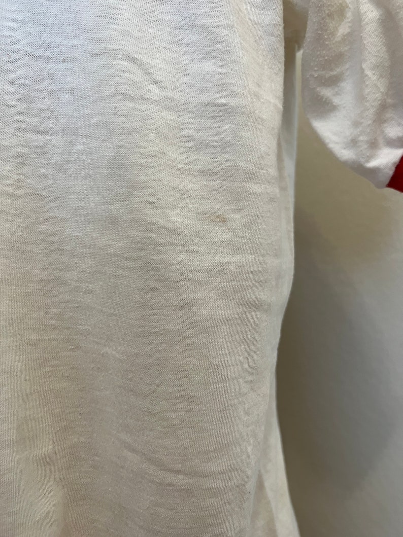 K&ouml;nnte beinhalten: Wei&szlig;es T-Shirt mit roten &Auml;rmelb&uuml;ndchen.