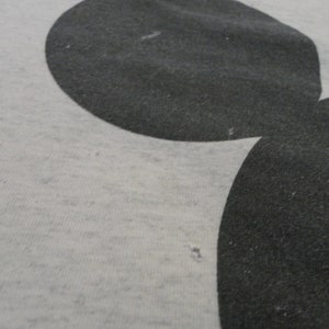 May include: A close-up of a gray t-shirt with a black Mickey Mouse silhouette printed on it.
