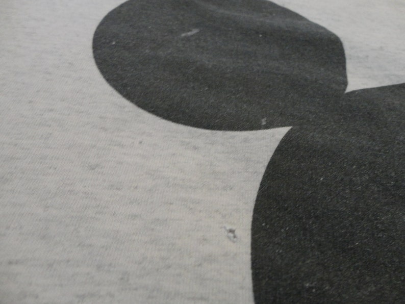 May include: A close-up of a gray t-shirt with a black Mickey Mouse silhouette printed on it.