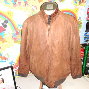 May include: A brown leather jacket with a zip-up front and a stand-up collar. The jacket has a bomber-style design with ribbed cuffs and hem. The jacket is displayed on a mannequin.