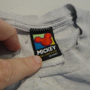May include: A gray t-shirt with a Mickey Mouse Unlimited tag. The tag is black with a colorful Mickey Mouse head and the text "Mickey Unlimited" and "&copy; Disney".