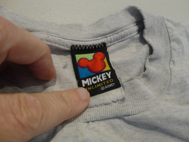 May include: A gray t-shirt with a Mickey Mouse Unlimited tag. The tag is black with a colorful Mickey Mouse head and the text "Mickey Unlimited" and "&copy; Disney".