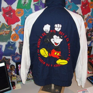 May include: Navy blue and white Mickey Mouse jacket. The back of the jacket features a large graphic of Mickey Mouse with the text "MICKEY & CO." in a circular design. The jacket has a high collar and raglan sleeves.