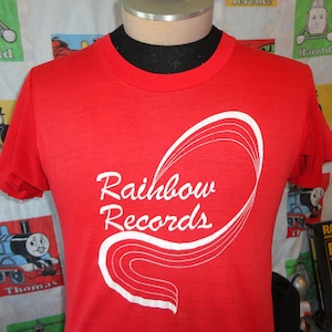 May include: Red t-shirt with a white graphic of a rainbow and the text "Rainbow Records".