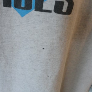 May include: A close-up of a gray t-shirt with two small holes in the fabric.