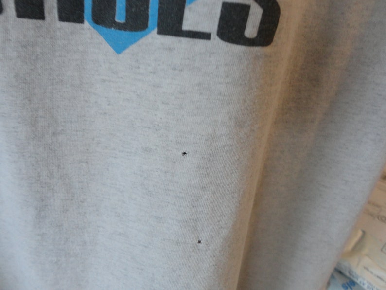 May include: A close-up of a gray t-shirt with two small holes in the fabric.