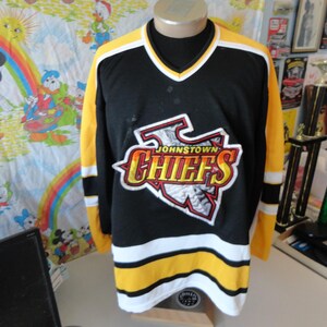 May include: Black and yellow hockey jersey with the words "Johnstown Chiefs" in a red, yellow, and white logo on the front.
