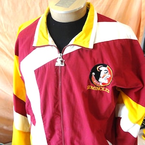 May include: A maroon, yellow, and white zip-up windbreaker jacket featuring the Florida State Seminoles logo on the chest. The jacket has a high collar, long sleeves with color-blocked panels, and a silver metal zipper pull with the Starter logo.
