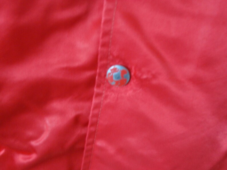 May include: A close-up of a red satin jacket with a single button closure. The button is silver with a design on it.