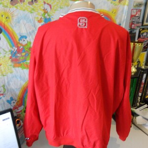May include: Red windbreaker jacket with a white zip and white trim around the collar and cuffs. The jacket has a white logo on the back that says "80".