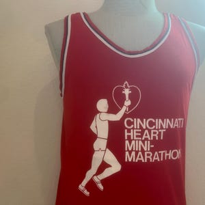 Peut inclure: Un débardeur rouge avec un graphique blanc d'un coureur tenant une torche et un cœur. Le texte "Cincinnati Heart Mini-Marathon" est imprimé sous le graphique.