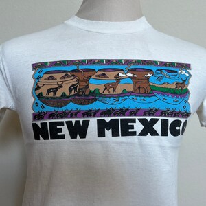 Può includere: Maglietta bianca con una grafica colorata di ceramiche native americane e il testo "NEW MEXICO".