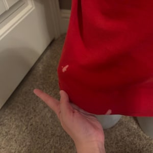 Op de afbeelding: Een close-up van een rood stofoppervlak met twee kleine witte vlekken. De stof is glad en lijkt van een zacht materiaal te zijn.