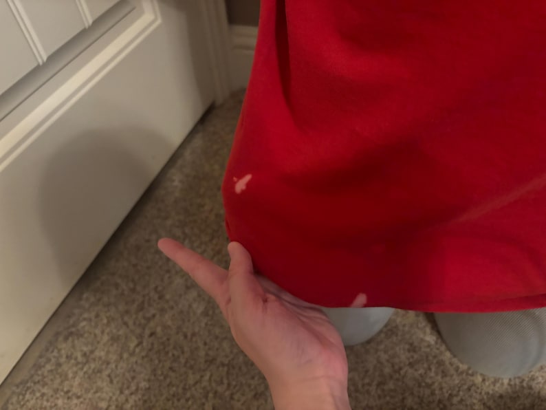 Op de afbeelding: Een close-up van een rood stofoppervlak met twee kleine witte vlekken. De stof is glad en lijkt van een zacht materiaal te zijn.