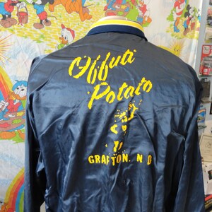 May include: A blue satin jacket with yellow lettering that reads "Grafton Potato" and "Grafton, ND".