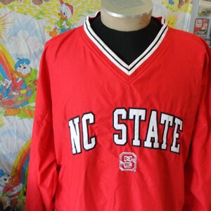 May include: Red windbreaker jacket with white NC STATE lettering and a red and white logo. The jacket has a black and white striped collar.