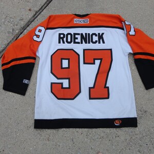 May include: A white hockey jersey with orange and black accents. The jersey features the name "ROENICK" and the number "97" in black and orange. The sleeves are orange with black stripes and cuffs. The number "9" is on the right sleeve.