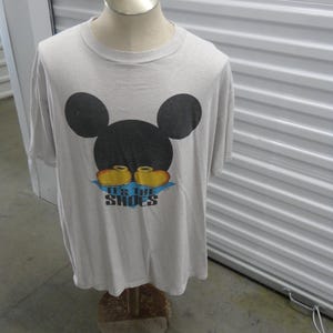 May include: A gray t-shirt with a black Mickey Mouse head and the text "It's the Shoes" in yellow and blue.