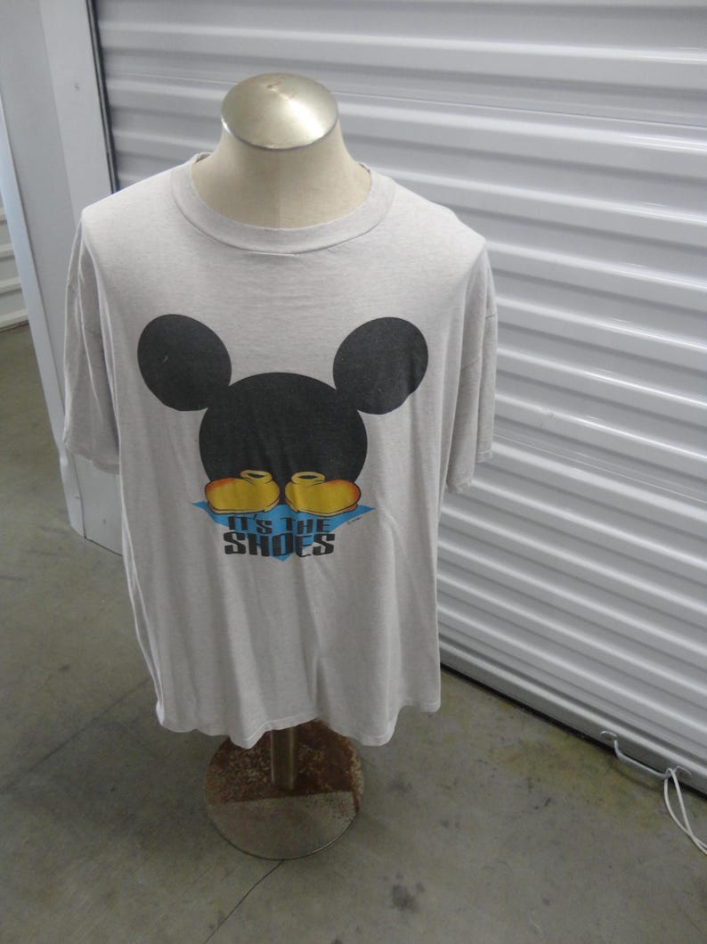 May include: A gray t-shirt with a black Mickey Mouse head and the text "It's the Shoes" in yellow and blue.