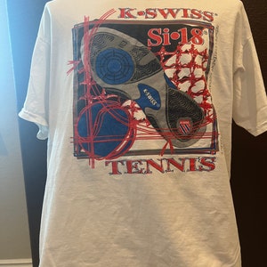 May include: White t-shirt with a red, blue, and black graphic of a tennis shoe with the text "K-SWISS Si-18 TENNIS" on the back.