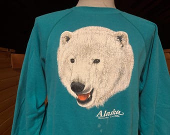 May include: Teal blue sweatshirt with a white polar bear graphic and the text "Alaska" in a white cursive font.