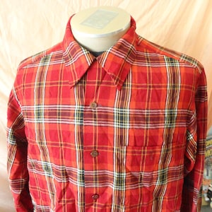 May include: A red plaid button-down shirt with long sleeves. The shirt features a classic plaid pattern in shades of red, orange, yellow, black, and white. It has a chest pocket and a collared neckline. The shirt is displayed on a mannequin.