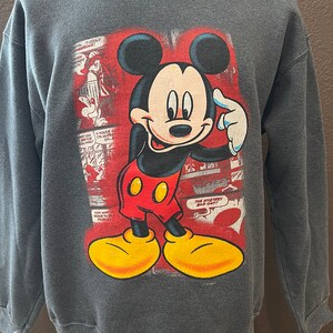 May include: A gray sweatshirt with a vintage Mickey Mouse graphic. The graphic features Mickey Mouse in a red and yellow outfit, with a red background and comic book style text. The text reads "The Mystery Bad Guy!"