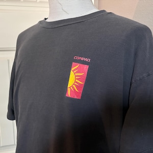 May include: Black t-shirt with a red and yellow sun graphic and the word "COMPAQ" printed on the front.