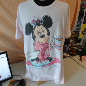 May include: A light pink t-shirt featuring a cartoon Minnie Mouse in a pink robe, holding a cup. The text "Time for more Beauty Sleep" is below the image. The shirt is displayed on a mannequin.