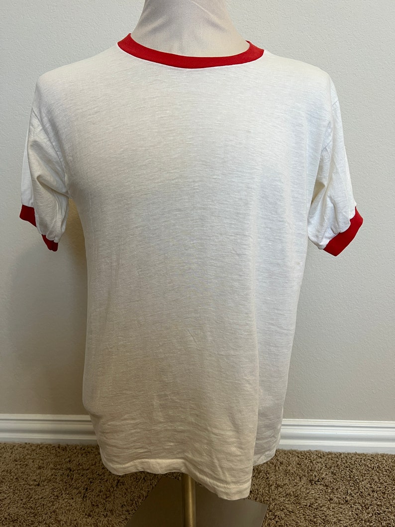 K&ouml;nnte beinhalten: Wei&szlig;es T-Shirt mit rotem Besatz an Kragen und &Auml;rmeln.