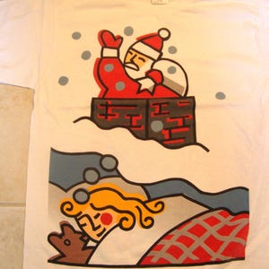 May include: White t-shirt with a colorful graphic of Santa Claus in a chimney, with a sleeping figure below. Santa is wearing a red suit and hat, with gray snowflakes. The sleeping figure has blonde hair and is under a red and gray blanket.