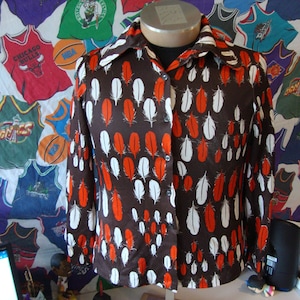 Puede incluir: Una camisa marrón de manga larga con cuello abotonado y un patrón de plumas blancas y naranjas.