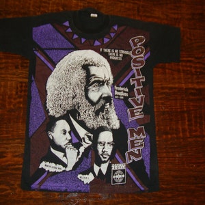 May include: Black t-shirt featuring a graphic of Frederick Douglass and other historical figures. The design includes the text "POSITIVE MEN" and "IF THERE IS NO STRUGGLE THERE IS NO PROGRESS". The shirt has a crew neck.