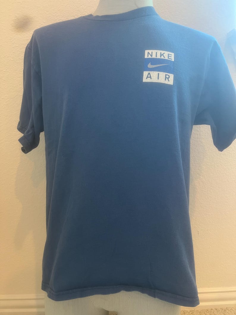 Puede incluir: Una camiseta azul con un logotipo blanco de Nike Air en la parte delantera.