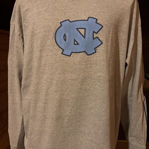 May include: A gray long-sleeve t-shirt with a blue UNC logo and a Nike swoosh on the chest.