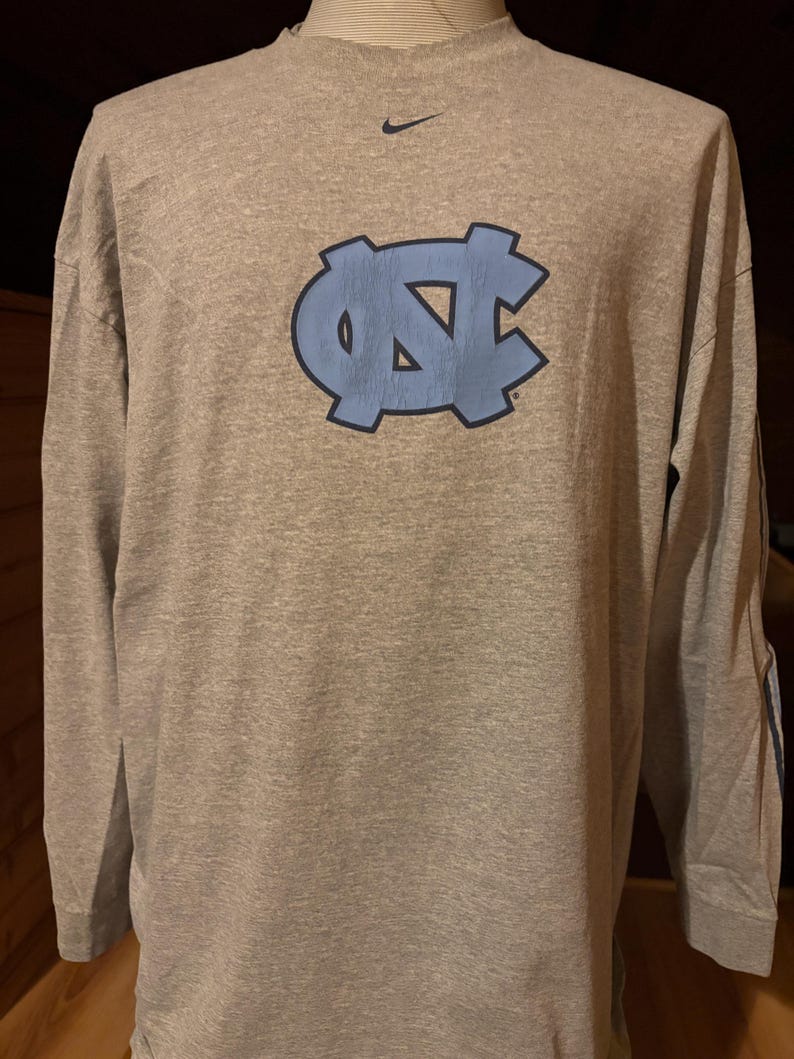 May include: A gray long-sleeve t-shirt with a blue UNC logo and a Nike swoosh on the chest.