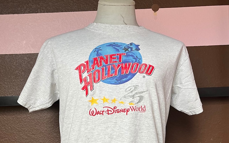 May include: A gray t-shirt with a red and blue graphic of a globe with the text "Planet Hollywood" and "Walt Disney World" printed on it.