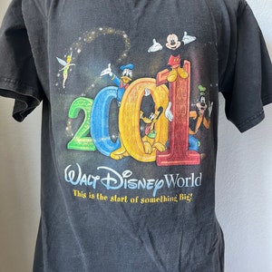 Puede incluir: Camiseta negra con un gr&aacute;fico de Mickey Mouse, Donald Duck, Goofy y Pluto celebrando el a&ntilde;o 2001 en Walt Disney World. El texto dice "Walt Disney World This is the start of something Big!"