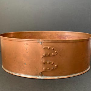 May include: A large, round copper planter with a hammered finish and two riveted seams on the side.