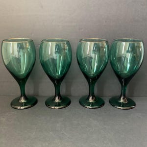 May include: Set of four green glass wine glasses with gold rims. The glasses have a classic shape and are perfect for serving wine or other beverages.