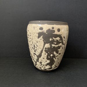 May include: A white ceramic vase with a brown and white abstract design. The vase has a rounded shape and a smooth finish.